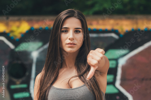 Portrait of a young woman showing thumbs down gesture over graffitit wall background photo