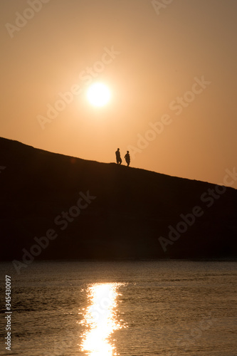 silhouette of two people walking on a hill at the beach at sunset