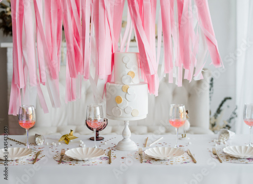 Party cake on decorated festive table. White holiday home interior. Birthday, wedding or baby shower decor. ?ibbon garland background. photo