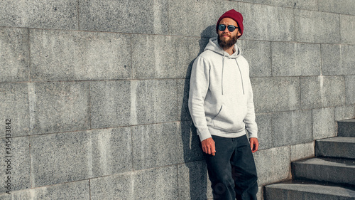 City portrait of handsome hipster guy with beard wearing gray blank hoodie or hoody with space for your logo or design. Mockup for print