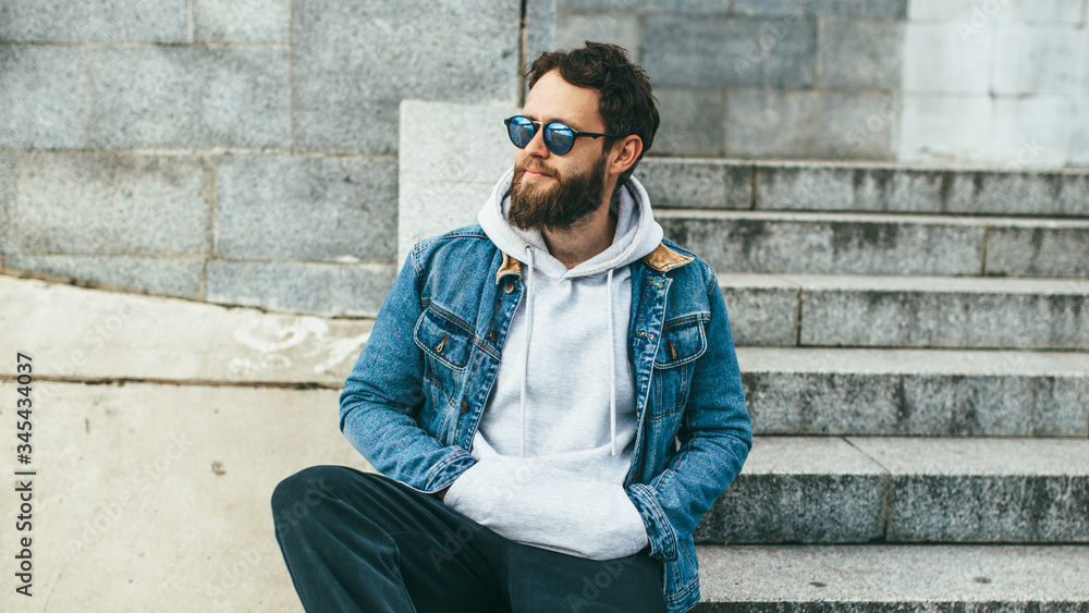 Obraz premium City portrait of handsome hipster guy with beard wearing gray blank hoodie or hoody with space for your logo or design. Mockup for print
