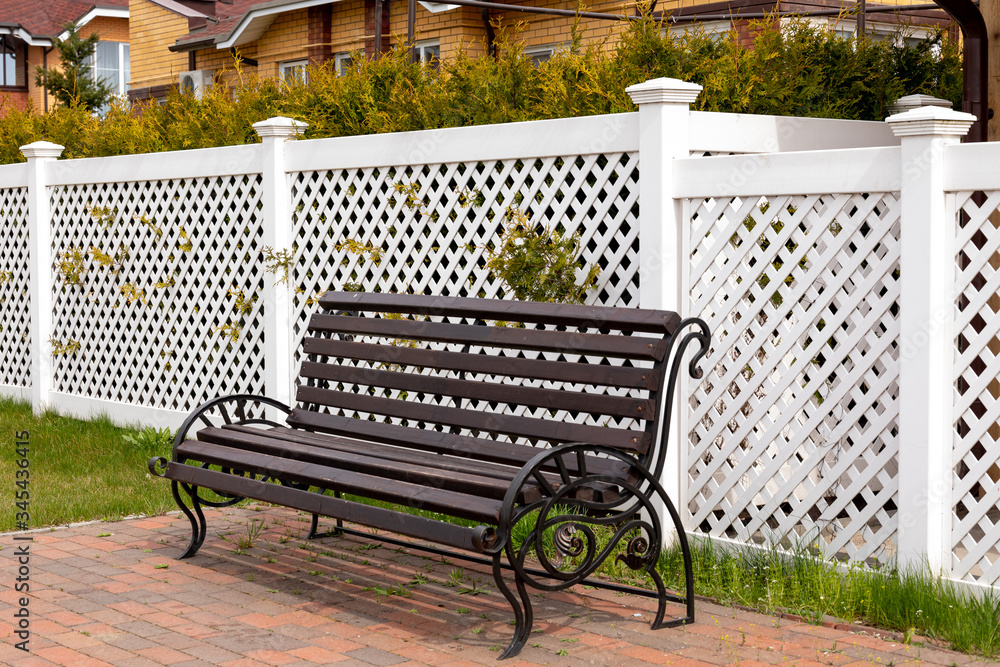 Empty dark wooden bench on the background of a white plastic fence in a rural village. Comfortable resting place under the open sky. Close-up, copy space. Empty dark wooden bench on the background of a white plastic fence in a rural village. Comfortable resting place under the open sky. Close-up, copy space.