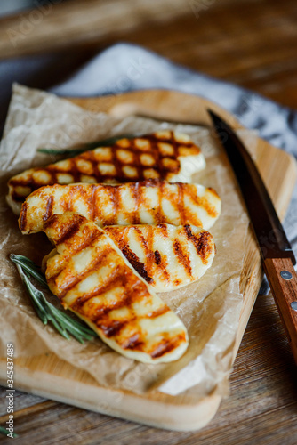 fried halloumi cheese with rosemary on a wooden cutting board on wooden table with wooden knife