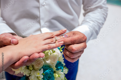 Bride and groom exchanging wedding rings close up during symbolic nautical decor destination wedding marriage on sandy beach in front of the ocean in Punta Cana, Dominican republic 