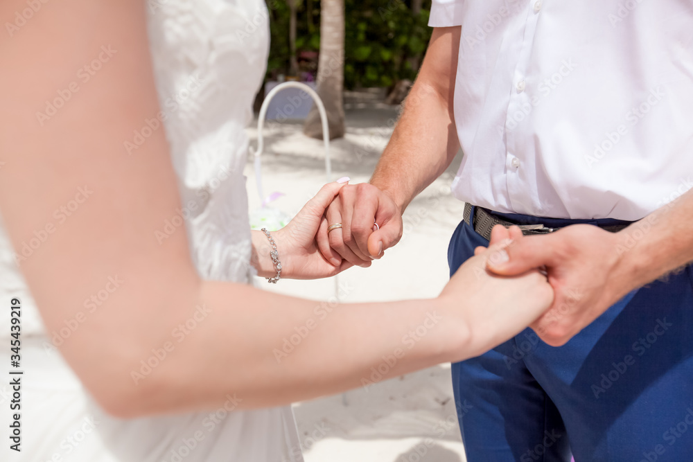 Fototapeta premium Bride and groom exchanging wedding rings close up during symbolic nautical decor destination wedding marriage on sandy beach in front of the ocean in Punta Cana, Dominican republic 