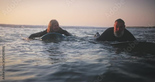 Senior man and woman surfing in the water at sunset