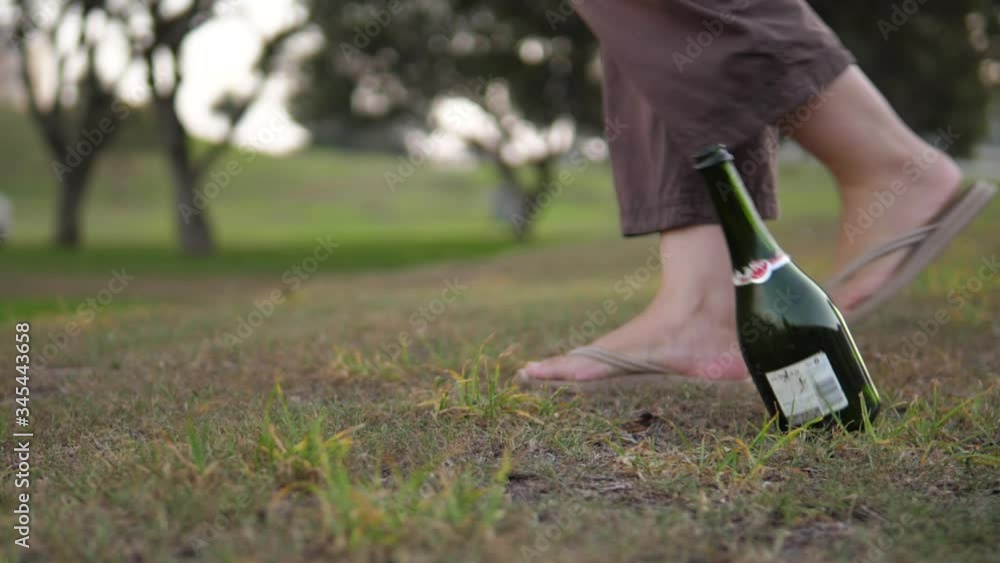 Dramatic slow motion shot of a socially irresponsible person tossing an empty wine bottle on the ground whilst walking in a public park. Dramatic slow motion shot of a socially irresponsible person tossing an empty wine bottle on the ground whilst walking in a public park.