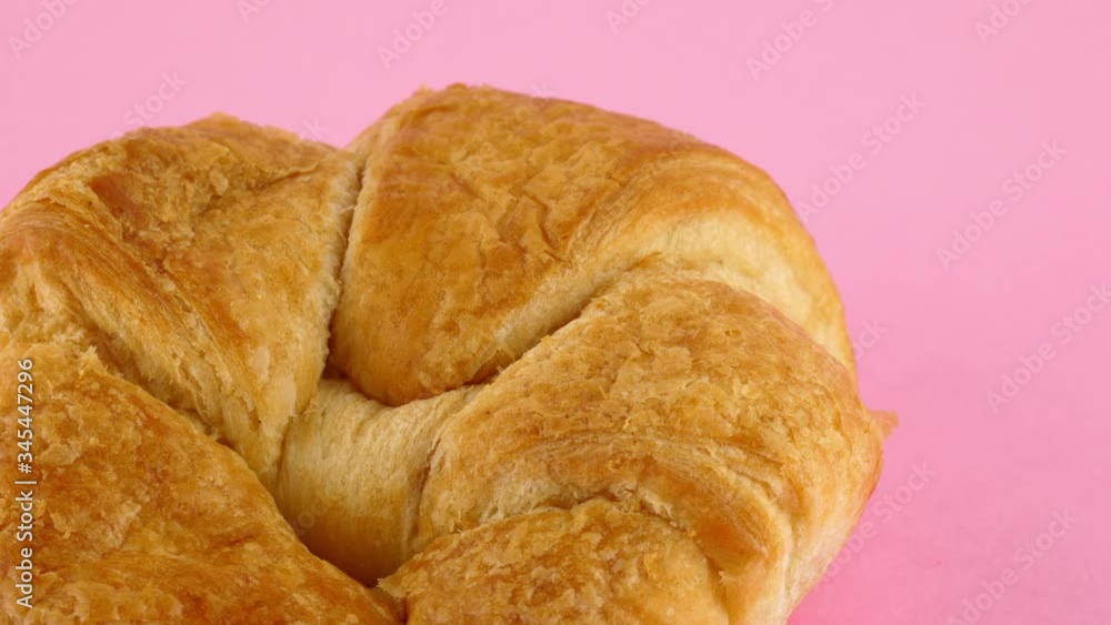 Rotating croissant against a pastel pink backdrop Rotating croissant against a pastel pink backdrop