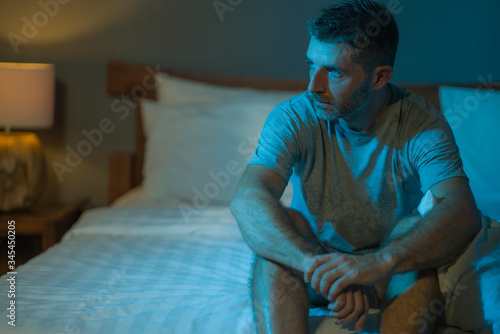 dramatic portrait in the dark of attractive depressed and worried man on bed suffering depression crisis and anxiety feeling lost sitting sleepless in insomnia and life problem concept