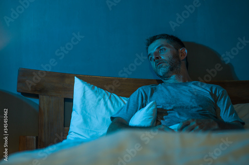 dramatic portrait in the dark of attractive depressed and worried man on bed suffering depression crisis and anxiety feeling lost lying sleepless in insomnia and life problem concept photo