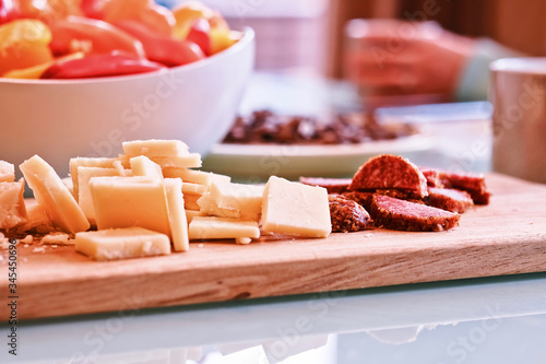 Cheddar cheese and sausage slices on wooden cutting board on dining table.