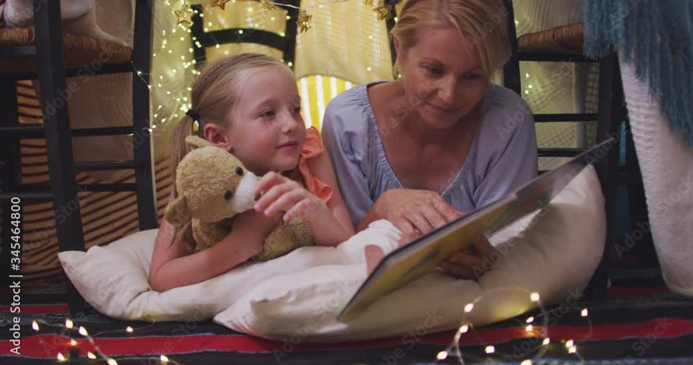 Front view of Caucasian woman reading a story to her daughter at home Front view of Caucasian woman reading a story to her daughter at home