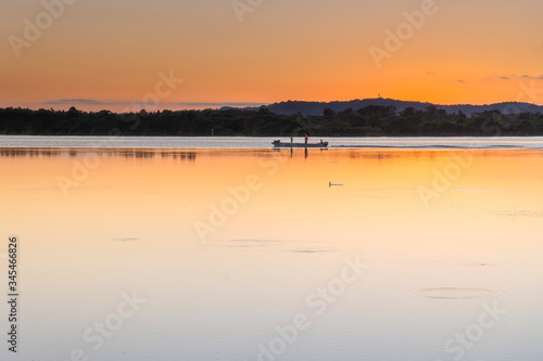 Soft Shades of an Orange Sunrise over the Bay with Three Fisherman in Boat