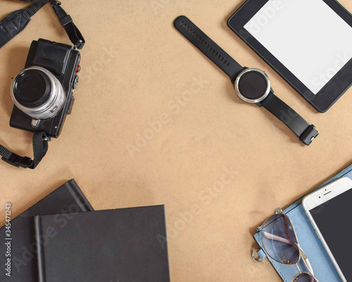 Top view of beach summer accessories with copy space. Travel must have such as a camera, notebook, tablet, watch, shade, and mobile phone. Copy space at the center. Wooden texture background