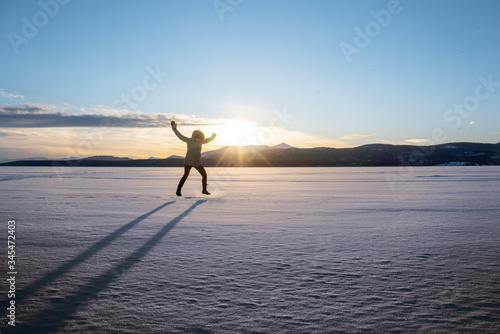 Silhouette of person woman jumping on frozen lake at sunset with mountains in the background. 