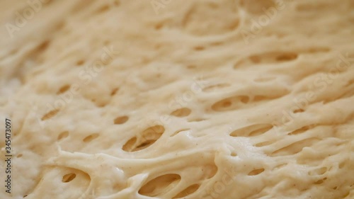 Macro shot of kneading rising bread dough. Bubbles of gluten stretch across the surface of the sourdough starter. Baking artisan bread from scratch is the hot food trend of the 2020 stay at home order
