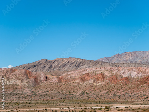 Scalloped striations of hillside erosion show layers of red rock.