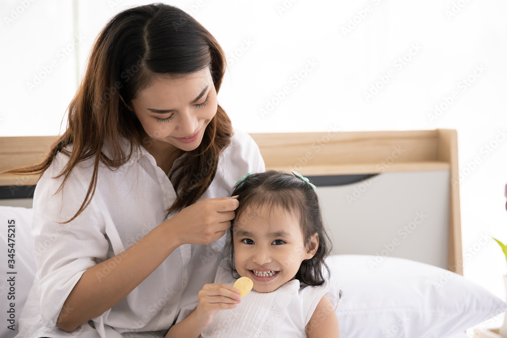 Happy Asian family. Single mother and Daughter aged three eat snacks on the bed in the house together Happy Asian family. Single mother and Daughter aged three eat snacks on the bed in the house together