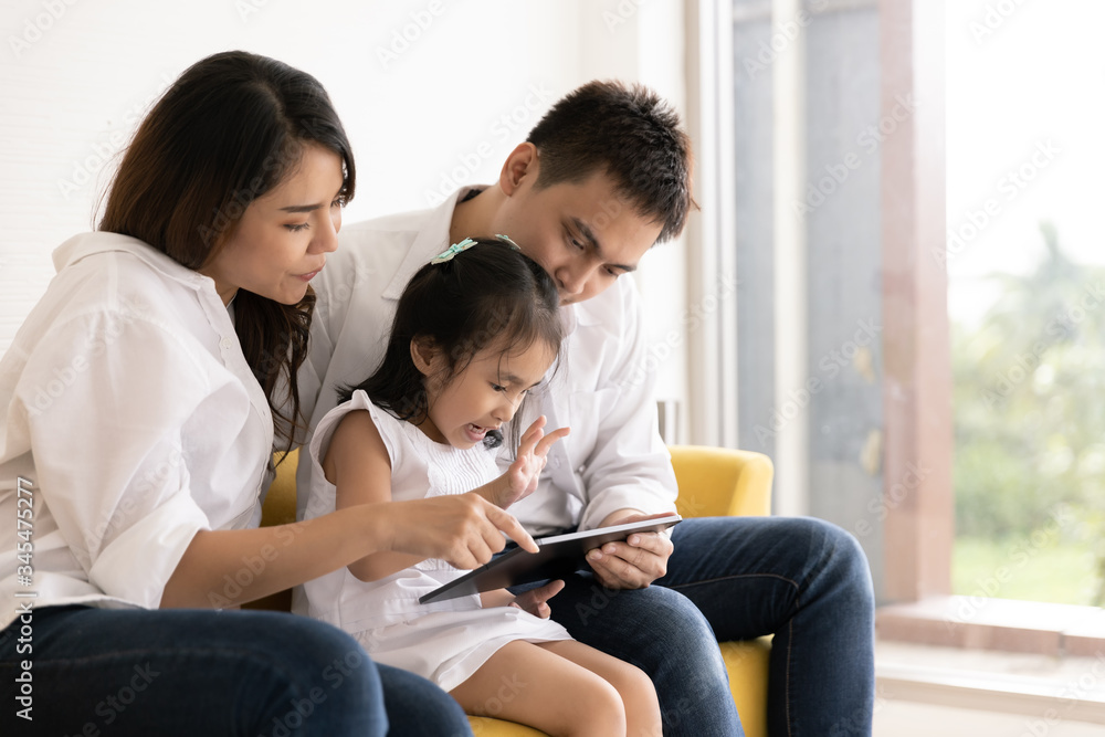 Happy Asian family using technologies for fun. Father, mother and daughter looking at digital tablet on sofa in the home. Communication technology and lifestyle Happy Asian family using technologies for fun. Father, mother and daughter looking at digital tablet on sofa in the home. Communication technology and lifestyle