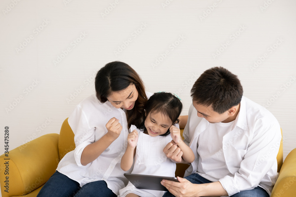 Happy Asian family using technologies for fun. Father, mother and daughter looking at digital tablet on sofa in the home. Communication technology and lifestyle Happy Asian family using technologies for fun. Father, mother and daughter looking at digital tablet on sofa in the home. Communication technology and lifestyle