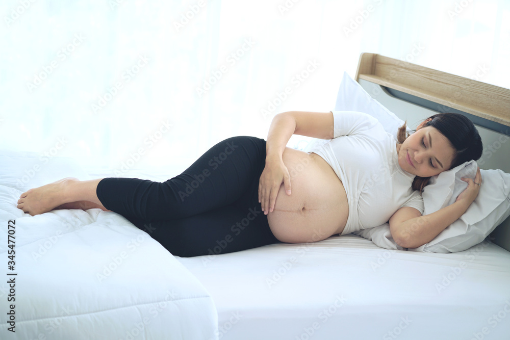 Asian pregnant women lie on their left side on bed Asian pregnant women lie on their left side on bed