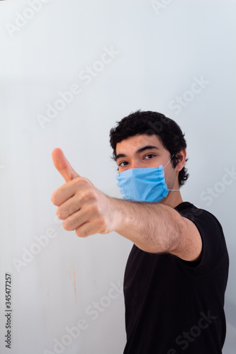 young man wearing a blue medical mask on a white background gesturing with his hands that everything will be fine