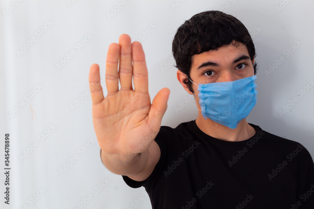 young man wearing a blue medical mask on a white background making the stop sign with his hands young man wearing a blue medical mask on a white background making the stop sign with his hands