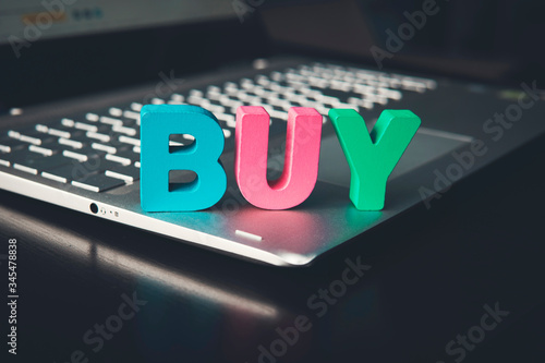 Buy word set on a laptop bottom contrasting on black desk. Business in internet. Online shopping. E-commerce. Wooden letters BUY ranged on notebook's keyboard. Motivation to purchase. Digital market. photo