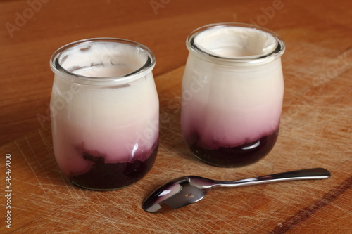 Yogurt with jam in open small glass jar with spoon on wooden cut