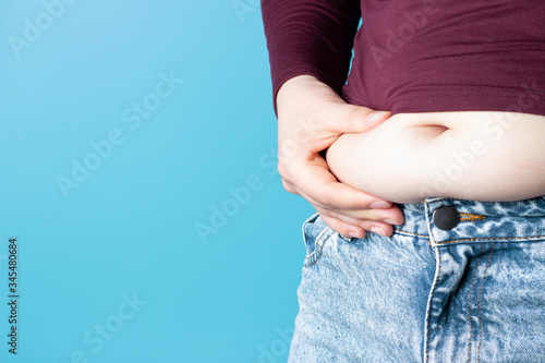 Tableau sur toile A woman's hand holds its belly on blue background, a side view, a copy of space,