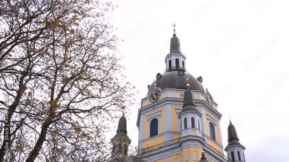 Church buildings roof hiding behind naked blossoming branches tree in the winter. Pan view in a cold and windy spring day in the park Church buildings roof hiding behind naked blossoming branches tree in the winter. Pan view in a cold and windy spring day in the park