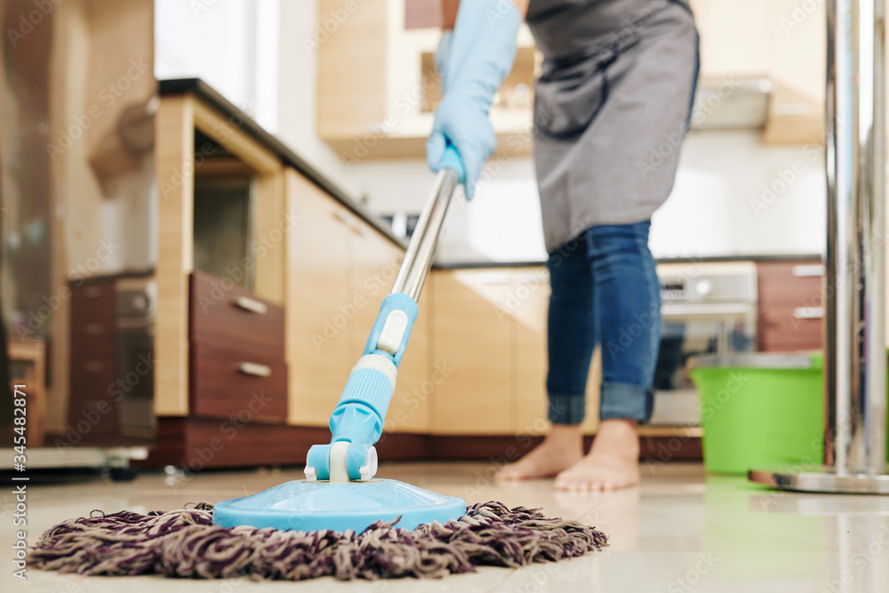 Fototapeta premium Housewife enjoying spring cleaning and mopping kitchen floor with mop, selective focus