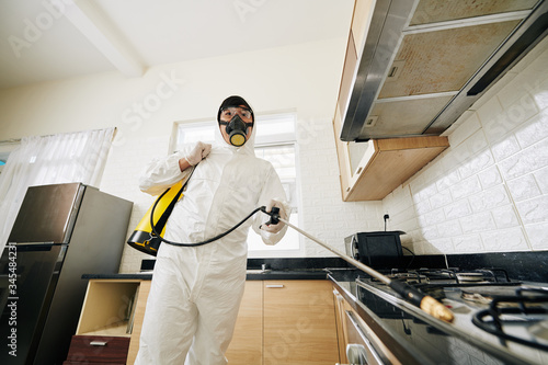 technician in protective suit and mask spraying chemicals in house to prevent spreding pneumonia virus photo