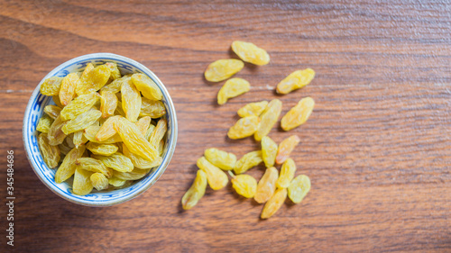 Top view of green raisins in a chinaware bowl with some raisins on brown wooden background. Copy space for text provided.