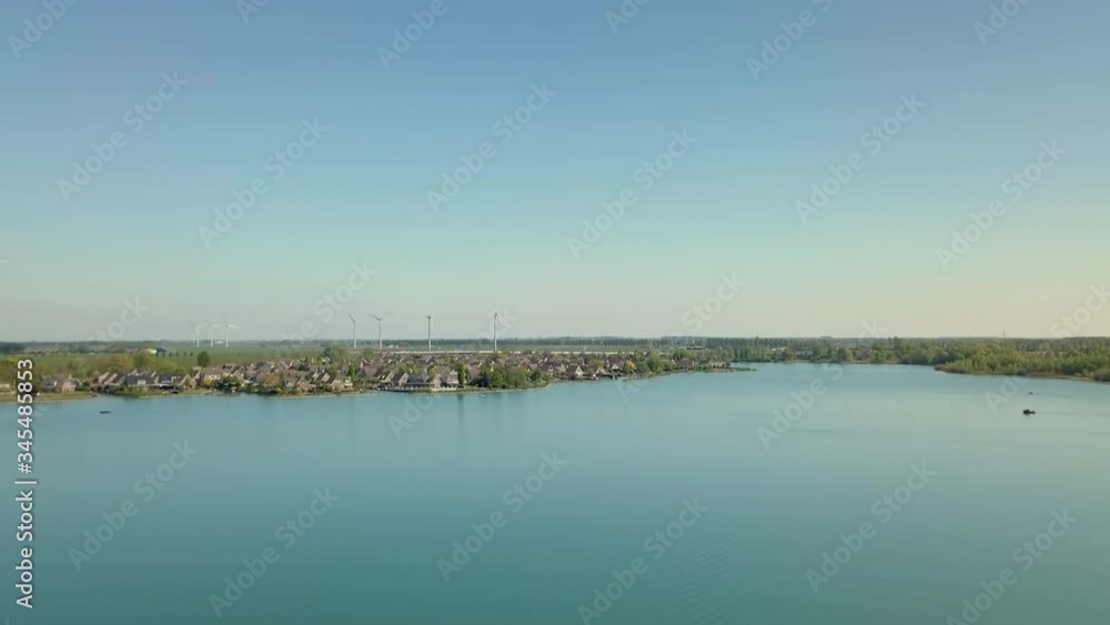 Aerial drone shot of flying up at the lake revealing the suburban and flat landscape with the wind turbines in the Netherlands. Aerial drone shot of flying up at the lake revealing the suburban and flat landscape with the wind turbines in the Netherlands.