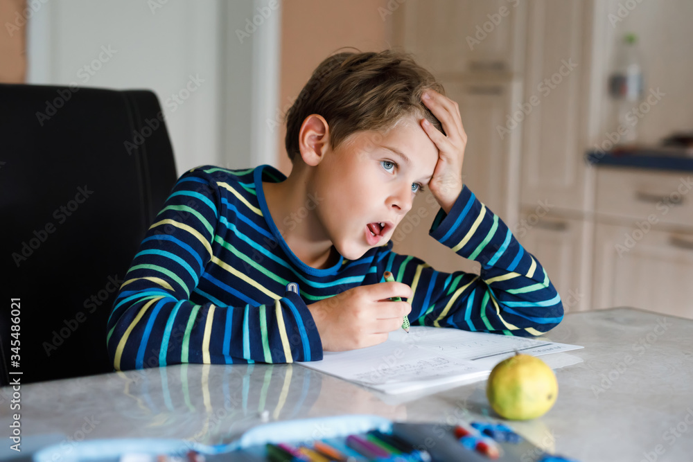 Hard-working happy school kid boy making homework during quarantine time from corona pandemic disease. Healthy child writing with pen, staying at home. Homeschooling concept Hard-working happy school kid boy making homework during quarantine time from corona pandemic disease. Healthy child writing with pen, staying at home. Homeschooling concept