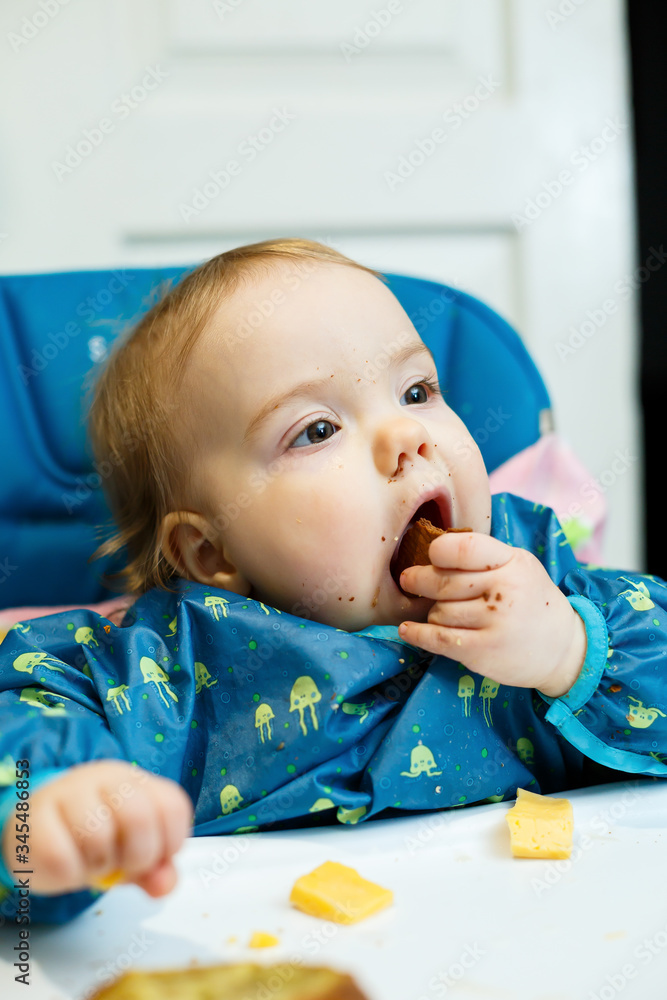 A small child sits in a feeding chair and eats bread for the first time. Face in crumbs A small child sits in a feeding chair and eats bread for the first time. Face in crumbs