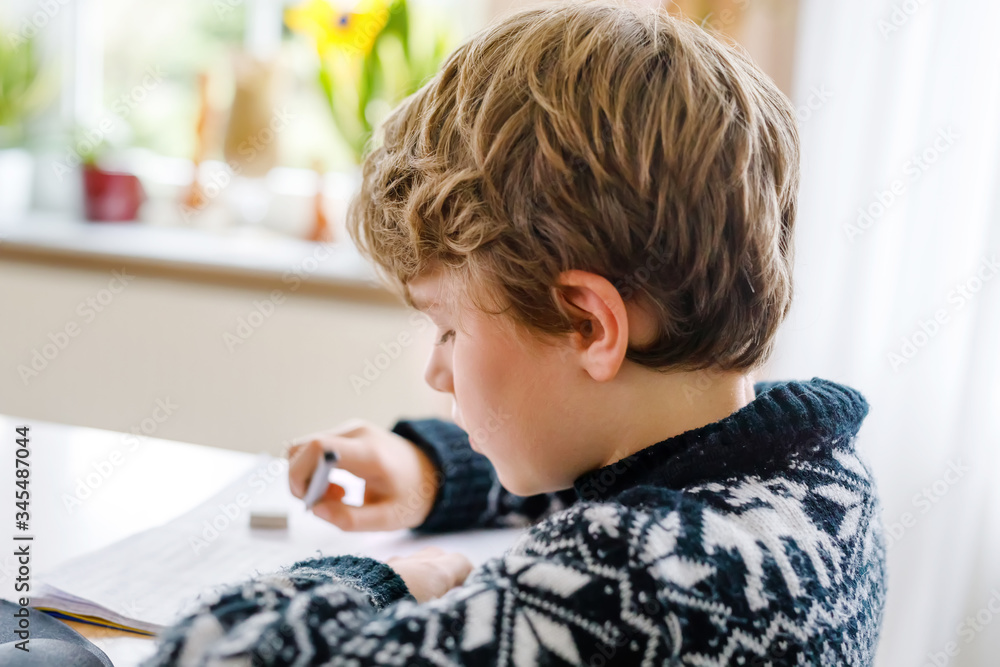 Hard-working happy school kid boy making homework during quarantine time from corona pandemic disease. Healthy child writing with pen, staying at home. Homeschooling concept Hard-working happy school kid boy making homework during quarantine time from corona pandemic disease. Healthy child writing with pen, staying at home. Homeschooling concept