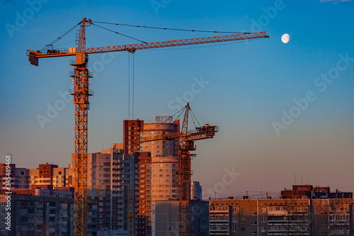 Tower cranes and houses in the city on sunset sky background
