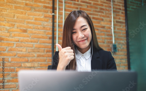 Принти на полотні Closeup image of a beautiful businesswoman showing thump up while using earphone