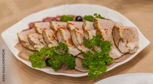 Sliced boiled meat and sprigs of parsley close up on a white plate on a tablecloth background