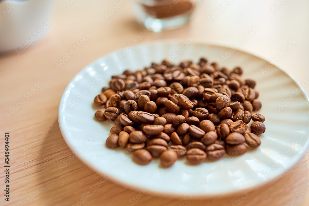 A white round plate with a handful of coffee beans is standing on the table. Selective focus A white round plate with a handful of coffee beans is standing on the table. Selective focus
