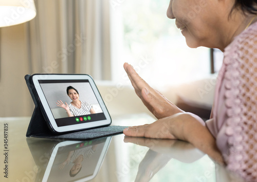 Fototapeta Naklejka Na Ścianę i Meble -  Asian Senior woman waving hand and talking to her relatives and family via internet and wireless technology. Old female making video call from home with digital tablet for meeting with young person
