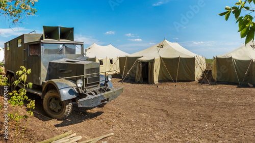 Retro german World War II military truck Krupp L3H163 is standing near a row of old canvas tents in a military camp photo