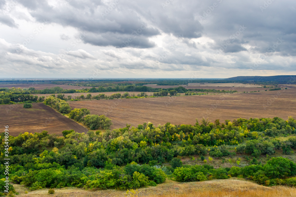 A landscape view with agricultural arable fields, forest shelterbelt and the rain cloudy sky