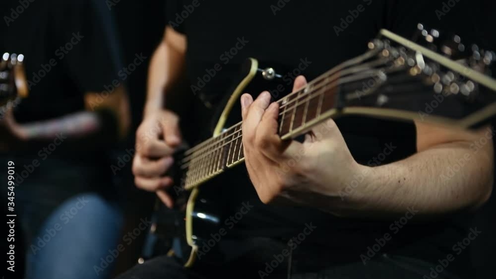 Two male guitarists in black clothes performing song in dark room. Two male guitarists in black clothes performing song in dark room.