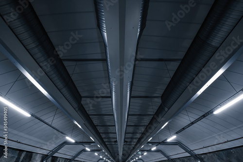 Sci fi looking dark and moody underground parking lot with fluorescent lights on.  Ceiling shot with ventilation tubes