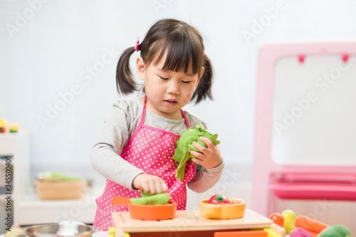 toddler girl pretend play food preparing role at home agianst white background