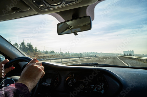 Windscreen view of nature, road, sky and hand of man on the steering wheel in a spring, summer or autumn day. The concept of a single trip