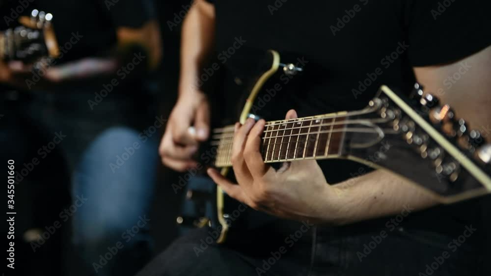 Two male guitarists in black clothes performing song in dark room. Two male guitarists in black clothes performing song in dark room.